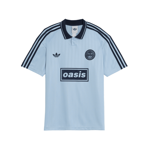 Light blue polo shirt with Adidas and Oasis logos on a green background