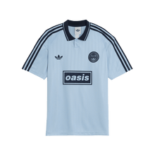 Light blue polo shirt with Adidas and Oasis logos on a green background